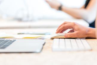 a person's hand moving a mouse with a laptop and keyboard nearby